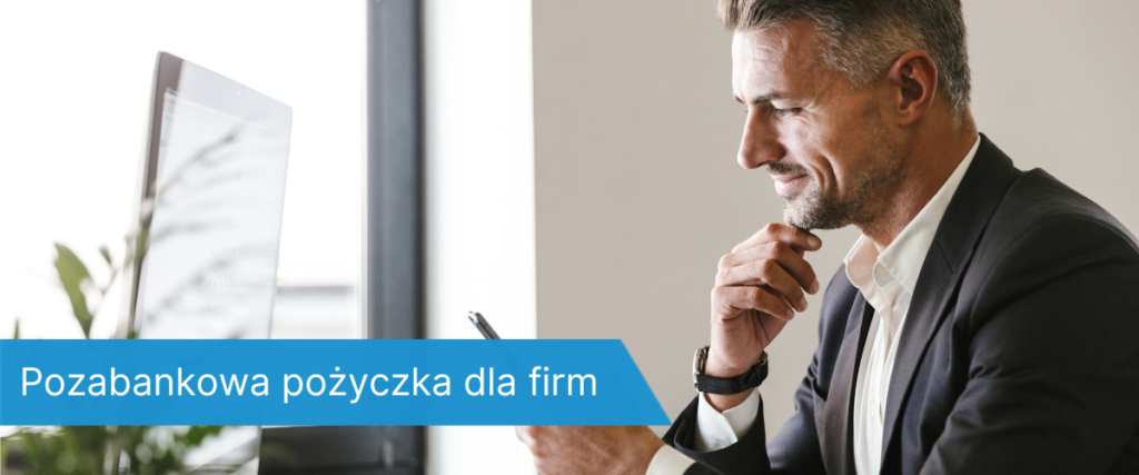 przedsiębiorca w ciemnym garniturze siedzący przy biurku, patrzy z uśmiechem na telefon